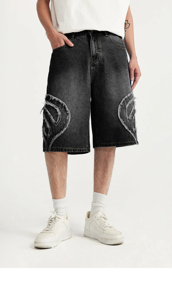 Model wearing the black Denim Patchwork Shorts in a gray background 